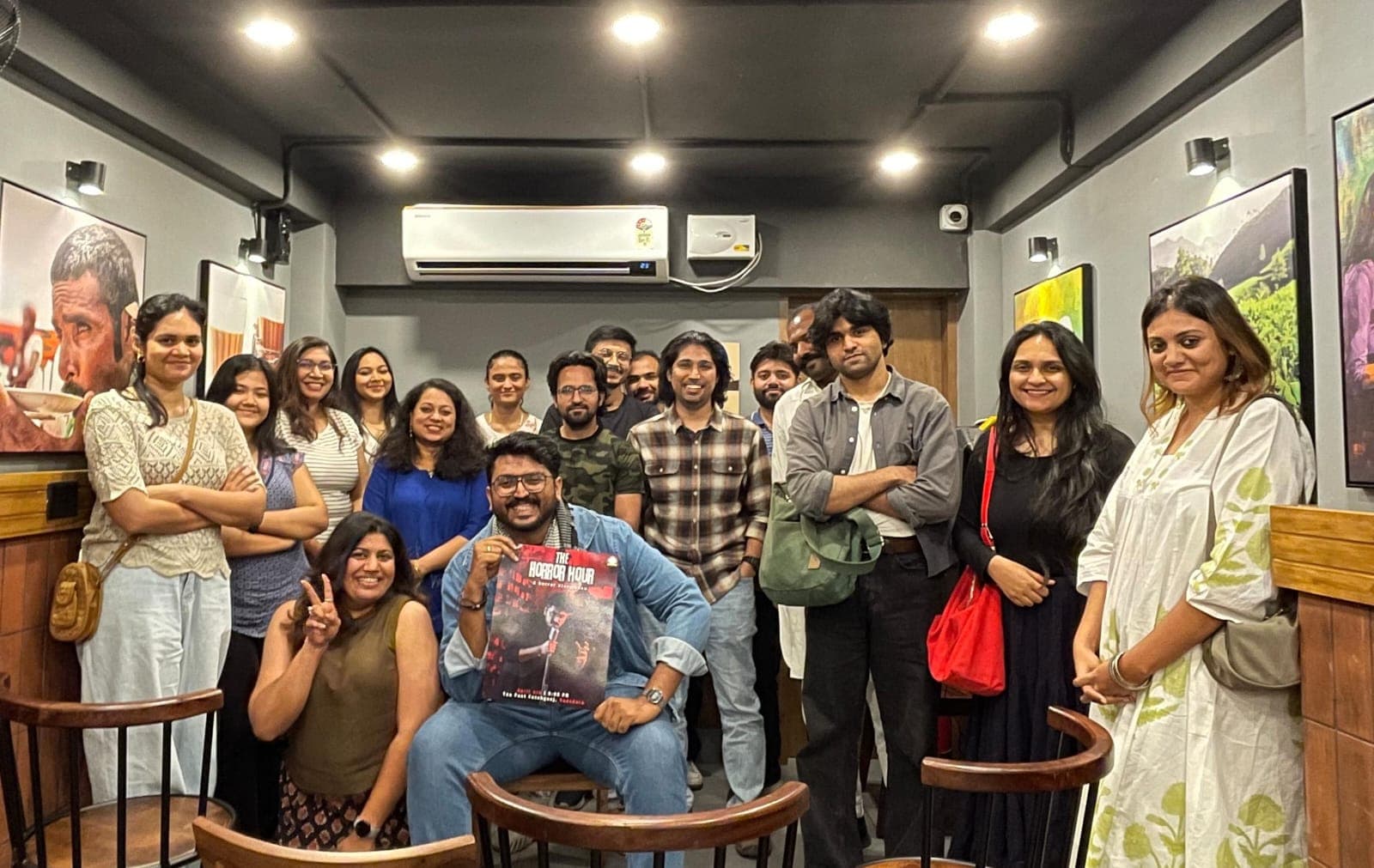 Horror Circle members at a cafe event holding The Horror Hour poster